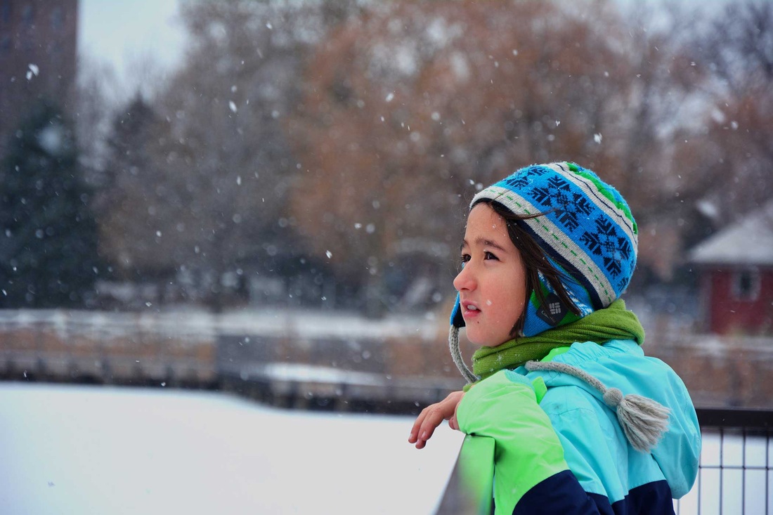 Child in a colorful winter coat watching falling snow