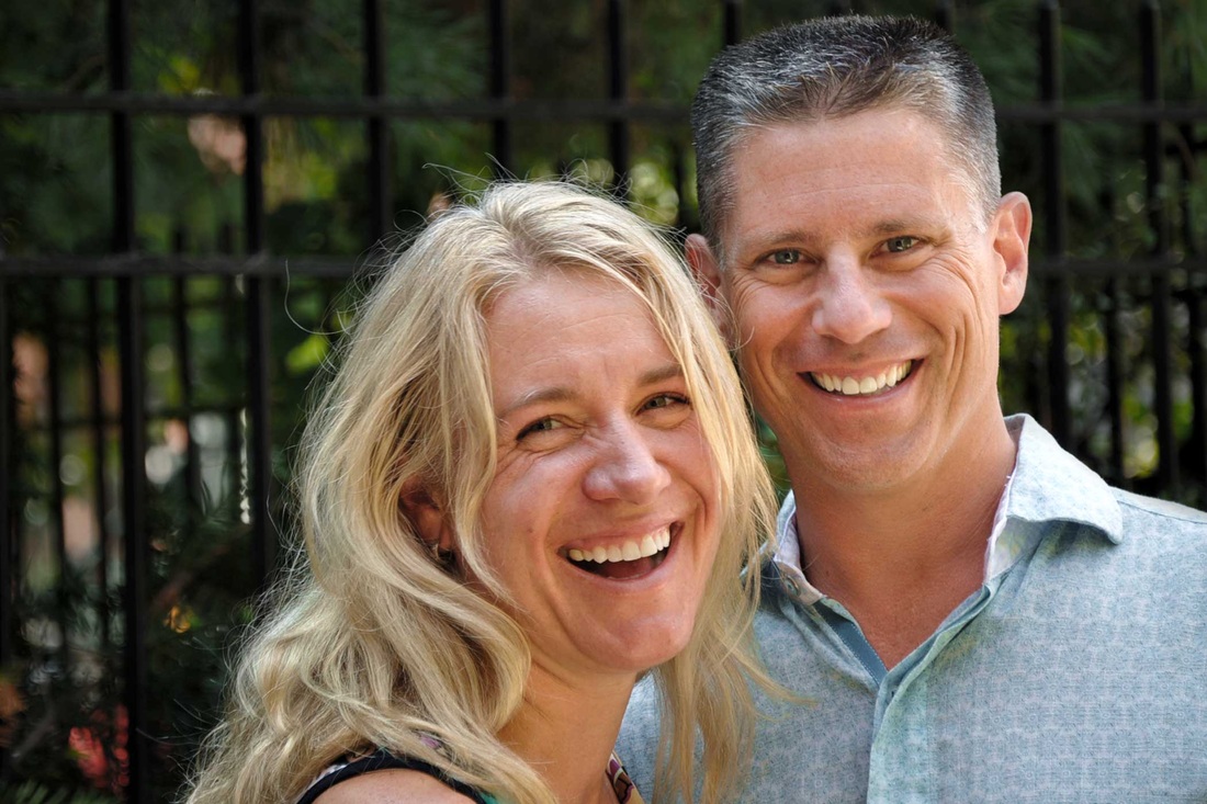 Two adults smiling together beside an outdoor fence